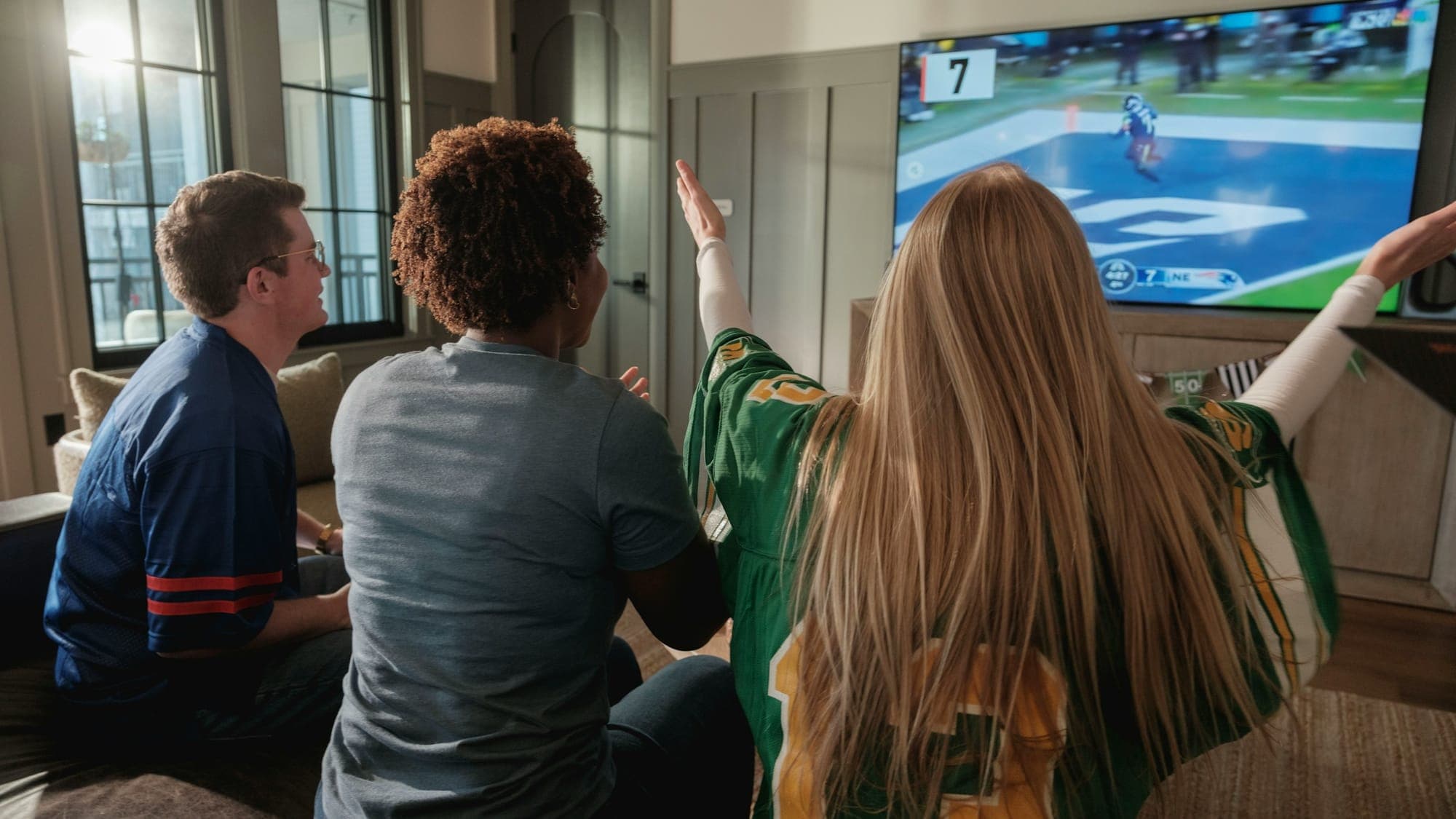 Friends in team jerseys watching an NFL game together on a living-room TV