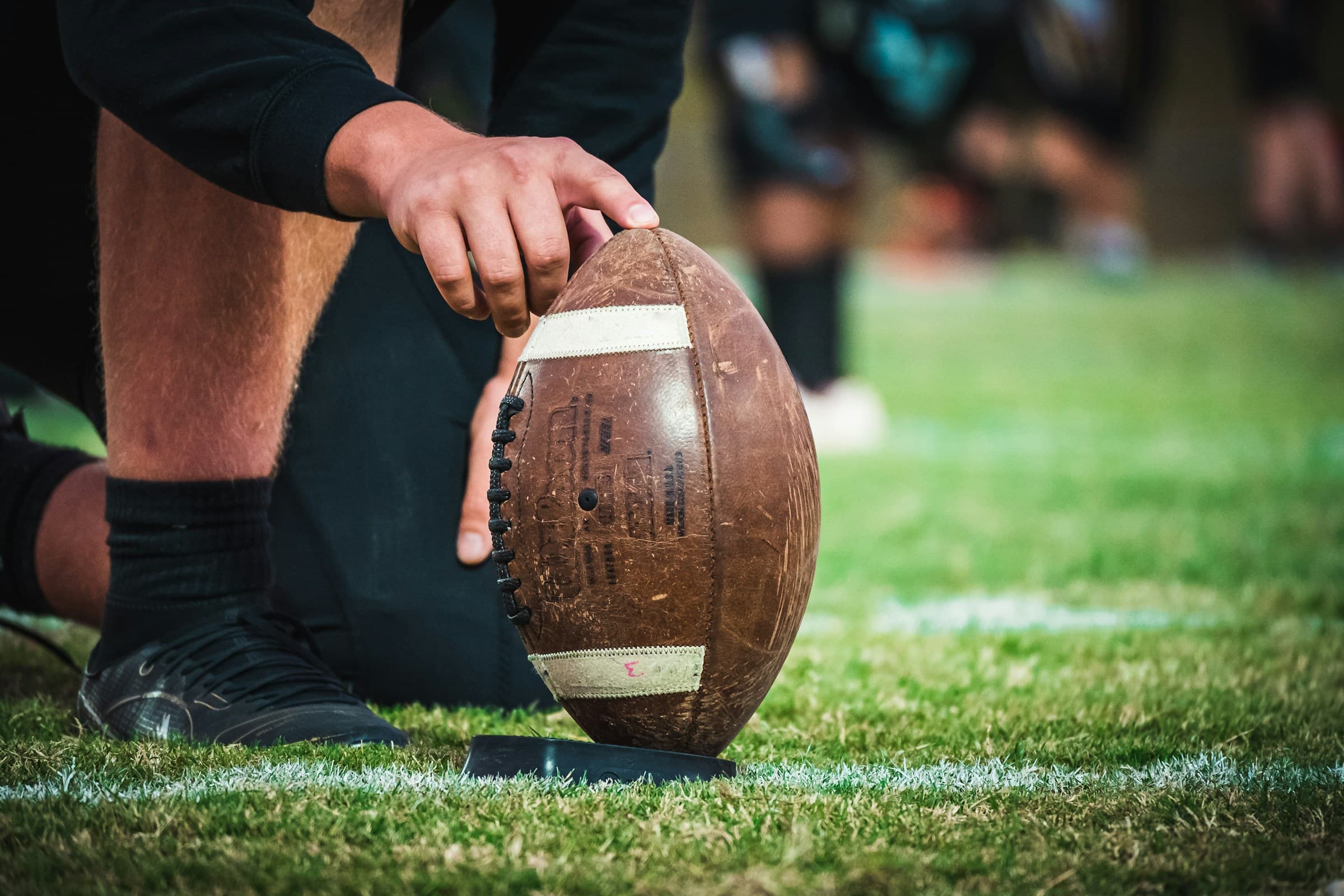 Close-up of a hand placing a football on a kicking tee on the field before a play